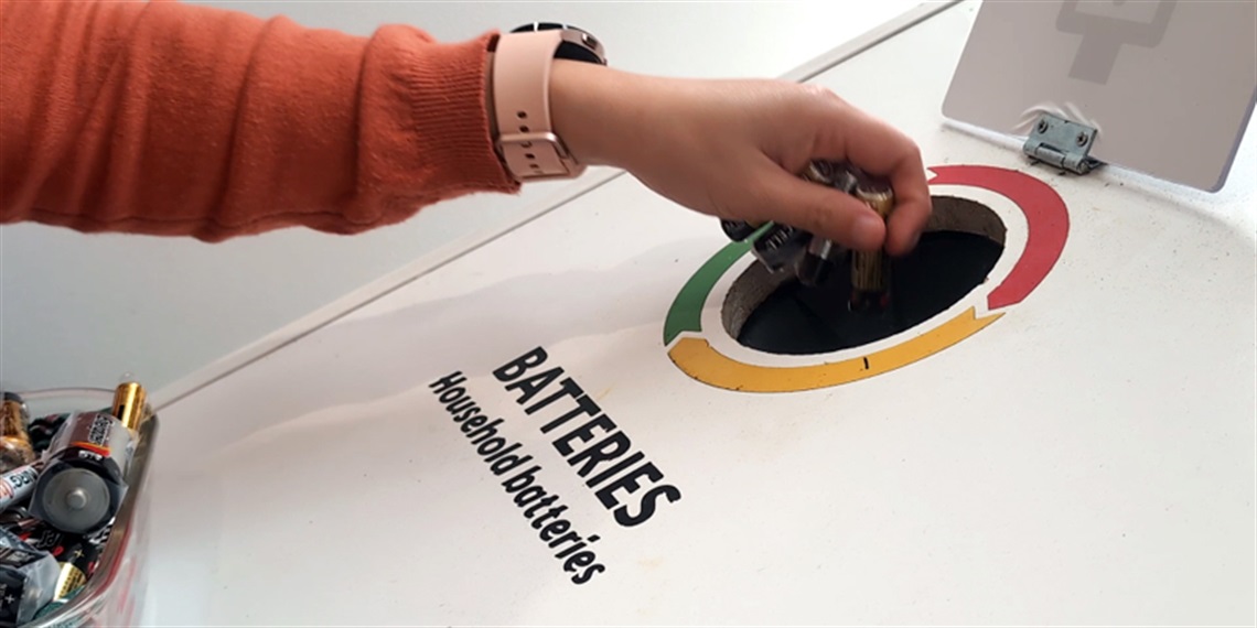 Photo of a person putting alkaline batteries into a problem waste station